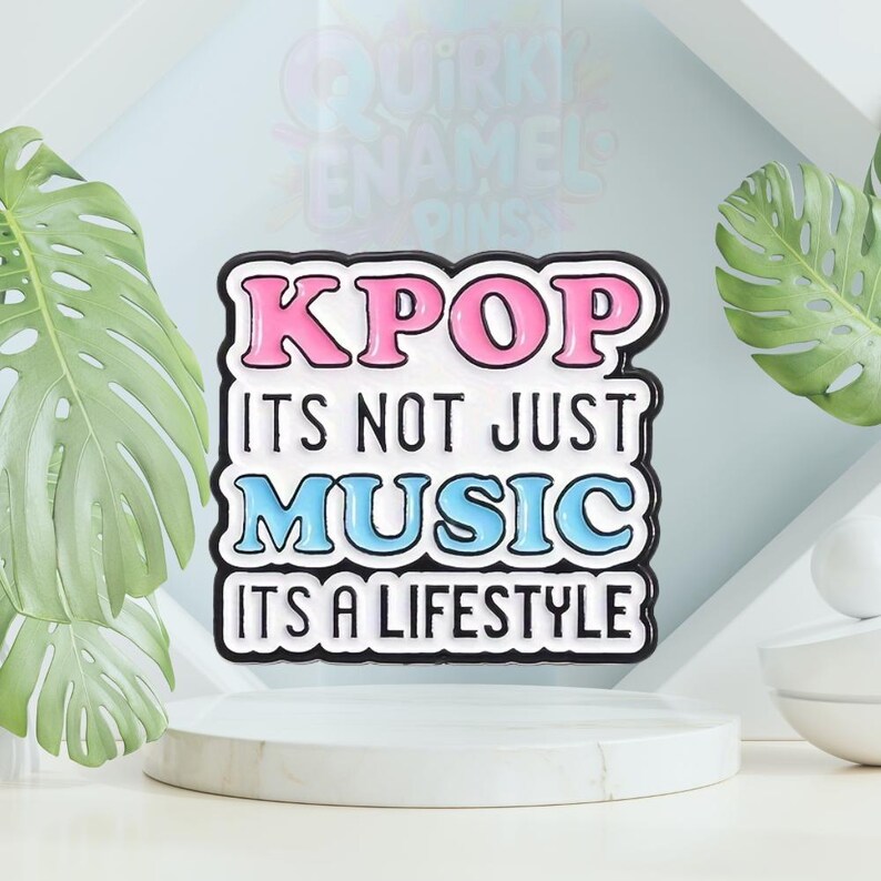 以下が含まれることがあります： 「KPOP ITS NOT JUST MUSIC ITS A LIFESTYLE」のテキストが入った長方形のエナメルピン。ピンは黒い縁取りで、「KPOP」はピンク、「MUSIC」は青、残りは白で書かれています。