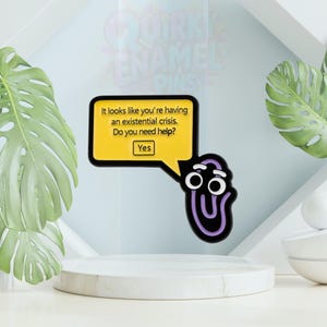 May include: A novelty enamel pin with a purple paperclip design and a yellow speech bubble. The speech bubble reads: "It looks like you're having an existential crisis. Do you need help? Yes." The pin is part of the "QUIRKY ENAMEL PINS" collection.