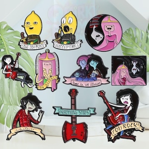 May include: A selection of enamel pins inspired by Adventure Time, featuring characters and quotes. The pins depict characters like Lemon Grab and Marceline, with phrases including "Unacceptable" and "Everything Stays".