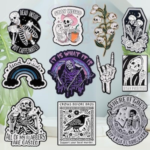 May include: A selection of black and white stickers featuring skeleton and gothic designs. The stickers depict a skeleton drinking coffee, a skeleton with a cowboy hat, a rainbow, a grim reaper, and a crow. Text includes "Dead Inside", "Stay Weird", and "Crows Before Bros".