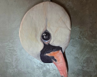 May include: A round, stuffed fabric wall hanging featuring a detailed, realistic print of a white swan head. The swan has a dark eye, a black beak base, and a pinkish-orange beak tip. A beige fabric loop is attached to the top for hanging.