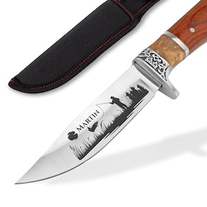 Può includere: Un coltello da caccia personalizzato con manico in legno marrone e lama in acciaio inossidabile. La lama presenta un design inciso di una persona che pesca e il testo "MARTIN". Il coltello viene fornito con un fodero in pelle nera.