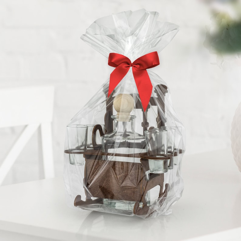 May include: A wooden liquor set with a bottle and four shot glasses, wrapped in clear plastic with a red bow. The set is shaped like a rocking chair.