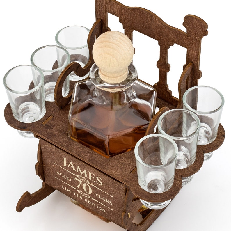 May include: A wooden liquor set with a decanter and six shot glasses. The set is shaped like a rocking chair and has the text "James Aged 70 Years Limited Edition" engraved on the front.