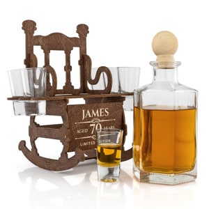 May include: Wooden rocking chair liquor dispenser with four shot glasses and a bottle of amber liquid. The dispenser is engraved with the text "JAMES AGED 70 YEARS LIMITED EDITION".