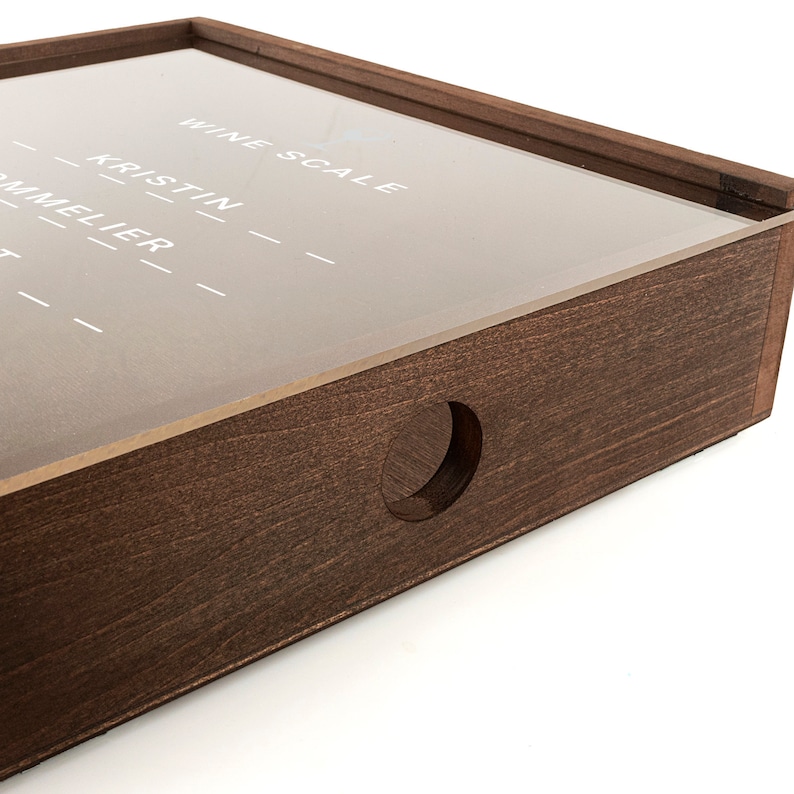 Puede incluir: Una caja de madera con una tapa de acr&iacute;lico transparente. La tapa tiene las palabras "Wine Scale" y "Kristin" escritas en ella. La caja tiene un agujero redondo cortado en el lateral.