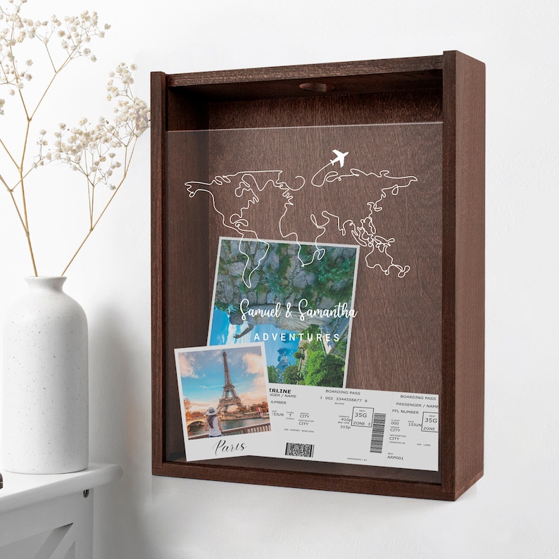 May include: A wooden shadow box with a clear acrylic front. The box contains a world map outline with a plane icon. There are two photos and a boarding pass inside the box. The photos show the Eiffel Tower in Paris, France. The boarding pass has the text "Samuel & Samantha Adventures".
