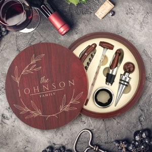 May include: A wooden box with a red finish and a gold inscription that reads "the JOHNSON FAMILY". The box contains a wine opener, a bottle stopper, a thermometer, and a foil cutter.