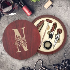 Peut inclure: Une boîte en bois avec une finition rouge et une lettre N dorée avec un motif floral. La boîte contient un tire-bouchon, un bouchon de bouteille, un thermomètre et un coupe-capsule.