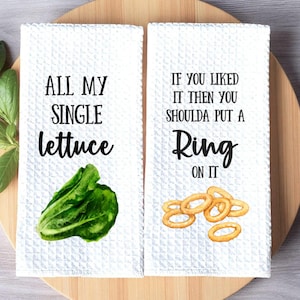 May include: Two white kitchen towels with the phrases "ALL MY SINGLE lettuce" and "IF YOU LIKED IT THEN YOU SHOULDA PUT A Ring ON IT". The first towel has a lettuce illustration, the second has onion rings.