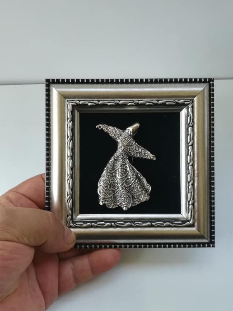 May include: A silver framed picture with a black velvet background featuring a silver 3D sculpture of a whirling dervish.