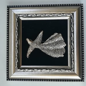 May include: A silver-colored, framed wall art piece depicting a whirling dervish figure with intricate calligraphy details. The figure is set against a black velvet background.
