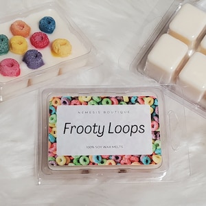 May include: A clear plastic container with six white wax melts shaped like cereal loops. The container has a label that says "Nemesis Boutique" and "Fruity Loops 100% Soy Wax Melts".