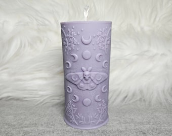 Puede incluir: Una vela de color lavanda con un diseño en relieve de una polilla, lunas y detalles florales.