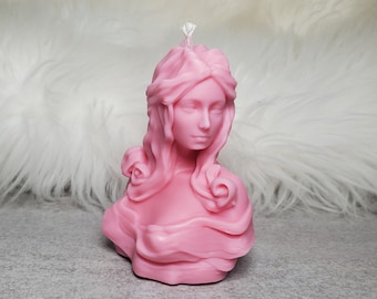 Könnte beinhalten: Eine rosa Kerze in Form einer Frauenbüste mit langen, fließenden Haaren. Die Kerze hat einen weißen Docht.