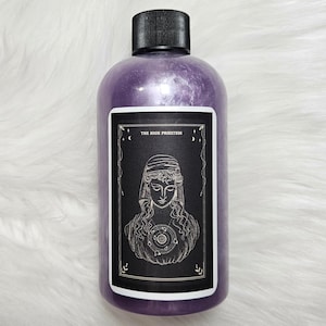 May include: A purple bottle with a black label featuring a tarot card illustration of The High Priestess. The label has a black background with gold accents and the text "THE HIGH PRIESTESS".