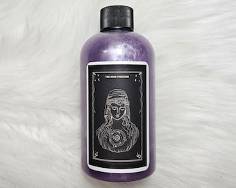 Könnte beinhalten: Eine violette Flasche mit einem schwarzen Etikett, das eine Tarotkarten-Illustration der Hohenpriesterin zeigt. Das Etikett hat einen schwarzen Hintergrund mit goldenen Akzenten und den Text "THE HIGH PRIESTESS".