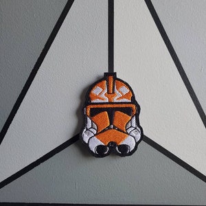 May include: An orange and white embroidered patch of a Star Wars clone trooper helmet.