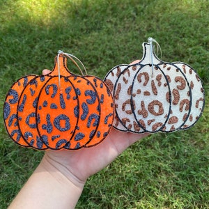 Pu&ograve; includere: Due decorazioni a forma di zucca con stampa leopardata glitterata. Una &egrave; arancione con macchie glitterate nere, l'altra &egrave; bianca con macchie glitterate marroni. Entrambe hanno ganci in filo d'argento.