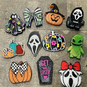 May include: A collection of Halloween-themed decorative charms. Includes a ghost, bow, pumpkin with witch hat, Scream mask, pumpkin with flowers, and a coffin with the text "GET IN LOSER".