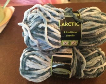 May include: Two skeins of Arctic chenille yarn in shades of blue, white, and gray. The yarn is labeled "A traditional chenille" and "A Jo-Ann exclusive!" on the packaging. Ideal for knitting and crochet projects.