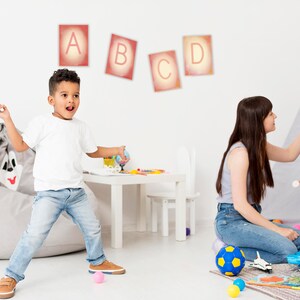 May include: A playroom with a grey beanbag chair, a white table and chair, and a teepee tent. Three children are playing with toys. The wall has colourful letters A, B, C, and D.