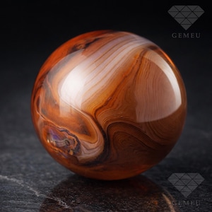 Peut inclure: Une pierre précieuse sphérique polie avec un motif tourbillonnant de bandes marron, orange et blanches. La pierre précieuse a une surface brillante et réfléchissante, et l'effet global est celui d'une beauté naturelle et de détails complexes. C'est un objet décoratif.
