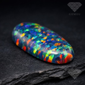 Könnte beinhalten: Ein polierter, ovaler schwarzer Opal-Edelstein. Der Opal zeigt ein lebendiges Farbspiel mit roten, orangen, gelben, grünen und blauen Blitzen. Der Edelstein liegt vor einem dunklen, strukturierten Hintergrund.