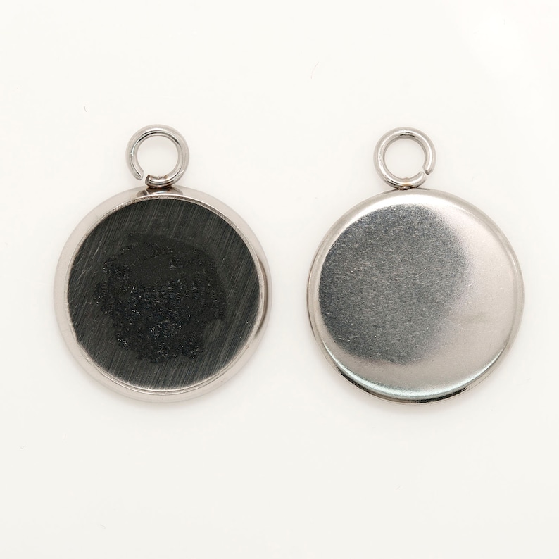 May include: Two silver round pendant charms with a loop at the top. One charm has a smooth surface and the other has a textured surface.