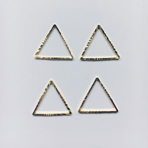 Puede incluir: Cuatro dijes de metal de forma triangular de color dorado con una superficie texturizada.
