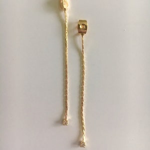 Puede incluir: Un par de pendientes de cadena de oro con un pequeño diamante al final de cada cadena.