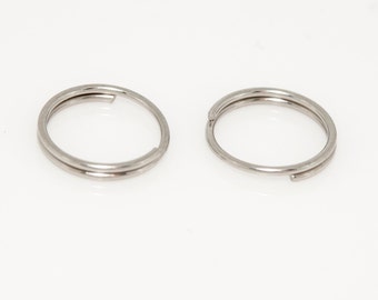 Puede incluir: Dos llaveros plateados, cada uno con forma circular y un diseño de doble bucle.