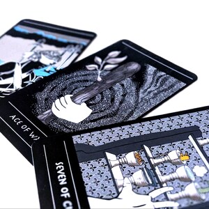 May include: Three tarot cards with black backgrounds and white illustrations. The cards are the Ace of Wands, Seven of Cups, and Ace of Swords. The Ace of Wands shows a hand holding a stick with a leaf growing from it. The Seven of Cups shows a hand reaching for a cup with a flame on top. The Ace of Swords shows a figure holding a sword.