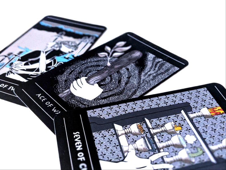May include: Three tarot cards with black backgrounds and white illustrations. The cards are the Ace of Wands, Seven of Cups, and Ace of Swords. The Ace of Wands shows a hand holding a stick with a leaf growing from it. The Seven of Cups shows a hand reaching for a cup with a flame on top. The Ace of Swords shows a figure holding a sword.