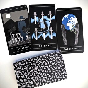 May include: Three tarot cards with black backgrounds and white text. The cards are "Eight of Cups", "Six of Swords", and "Two of Wands".