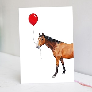 Könnte beinhalten: Aquarellillustration eines braunen Pferdes mit weißer Blesse, das einen roten Ballon hält. Das Pferd ist auf einer weißen Karte dargestellt, mit einem einfachen Design. Das Kunstwerk hat eine skurrile und charmante Ausstrahlung.