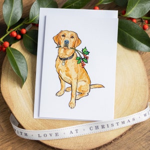 Peut inclure: Une carte de No&euml;l illustrant un chien golden retriever assis et tenant une branche de houx dans sa gueule, r&eacute;alis&eacute;e &agrave; l'aquarelle.