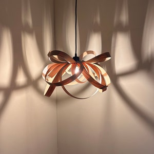 May include: A wooden pendant light fitting with a unique, interwoven design. The light fitting is hanging from a black cord and casts a warm glow.