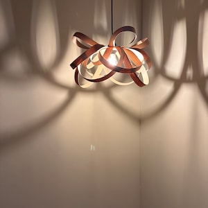 May include: A wooden pendant light fitting with a unique, interwoven design. The light fitting is hanging from a black cord and casts interesting shadows on the wall.