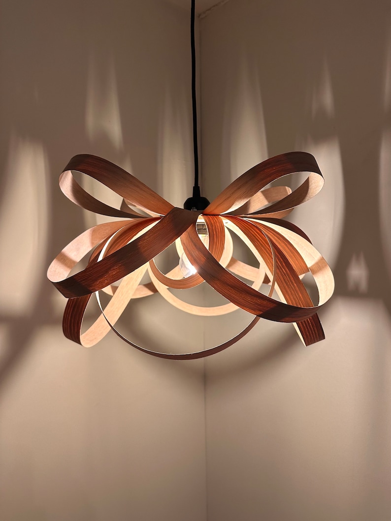 May include: A wooden pendant light fixture shaped like a bow. The light fixture is made of thin strips of wood that are woven together to create a unique and modern design.