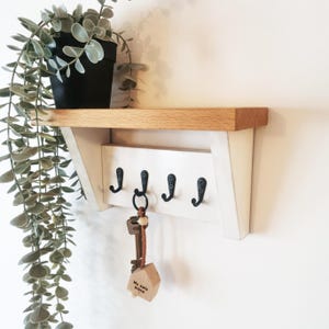 May include: White wooden key rack with a shelf on top. The rack has five hooks and a key ring with keys hanging from one of the hooks. The key ring has a small wooden tag that says "My safe place".
