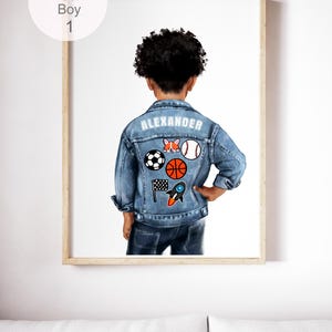 Könnte beinhalten: Ein gerahmter Druck, der ein Kind von hinten zeigt, das eine blaue Jeansjacke mit dem in weißen Buchstaben gedruckten Namen ALEXANDER trägt. Die Jacke ist mit Aufnähern eines Corgis, Baseballs, Fußballs, Basketballs, einer Flagge und einer Rakete verziert.
