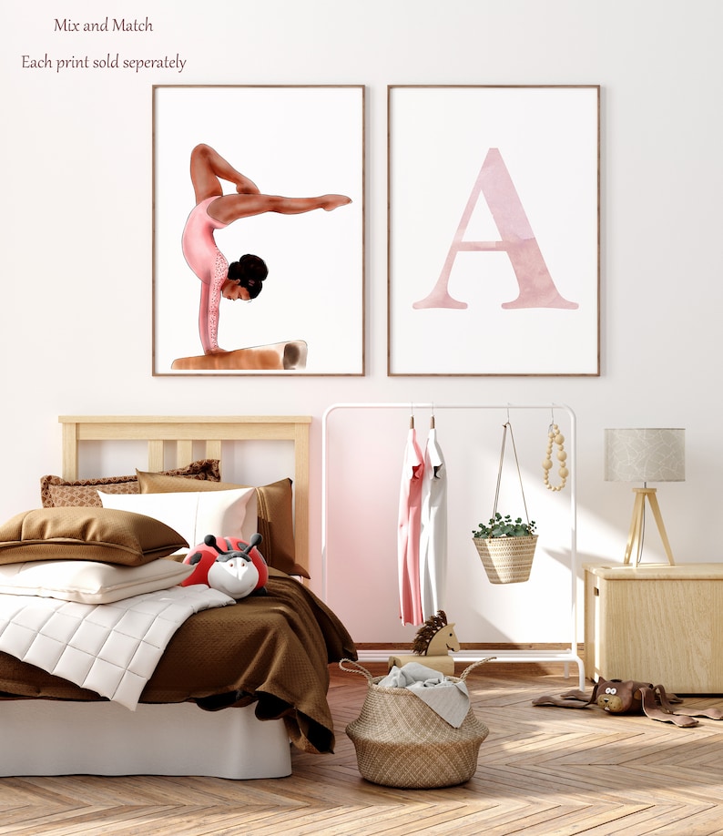 K&ouml;nnte beinhalten: Zwei gerahmte Drucke, einer mit einer Aquarellillustration einer Turnerin, die einen Handstand auf einem Schwebebalken macht, und der andere mit einer Aquarellillustration des Buchstabens A. Die Drucke h&auml;ngen an einer wei&szlig;en Wand &uuml;ber einem Holzbett mit braunen Bettw&auml;sche.