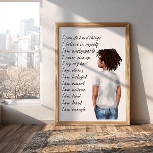 Könnte beinhalten: Ein gerahmter Kunstdruck mit einer Illustration einer Person mit dunklem Haar, die ein weißes T-Shirt und Jeans trägt und abgewandt ist. Der Druck enthält inspirierenden Text: "I can do hard things, I believe in myself, I am unstoppable..."