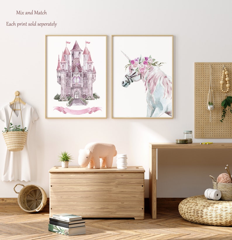 K&ouml;nnte beinhalten: Zwei Aquarelldrucke, einer von einem rosafarbenen Schloss und einer von einem Einhorn mit einer Blumenkrone. Die Drucke sind in hellem Holz gerahmt und an einer wei&szlig;en Wand aufgeh&auml;ngt. Der Text "Mix and Match" und "Each print sold separately" ist oben im Bild sichtbar.