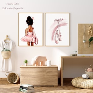K&ouml;nnte beinhalten: Zwei Aquarelldrucke, einer mit einer jungen Ballerina in einem rosa Tutu und der andere mit einem Paar rosa Ballettschuhen, die an einem rosa Band h&auml;ngen.