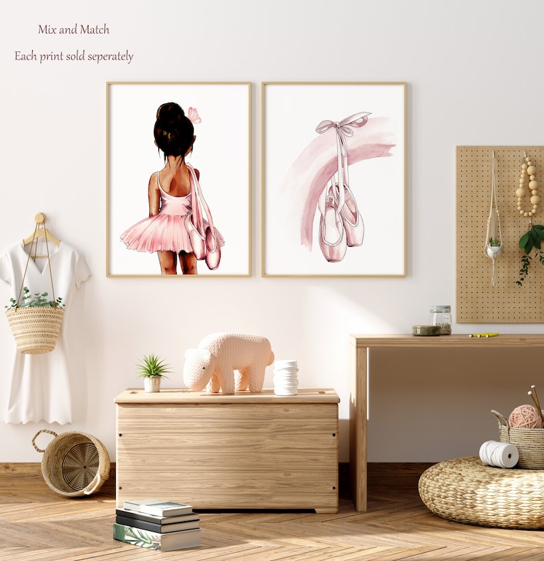K&ouml;nnte beinhalten: Zwei Aquarelldrucke, einer mit einer jungen Ballerina in einem rosa Tutu und der andere mit einem Paar rosa Ballettschuhen, die an einem rosa Band h&auml;ngen.