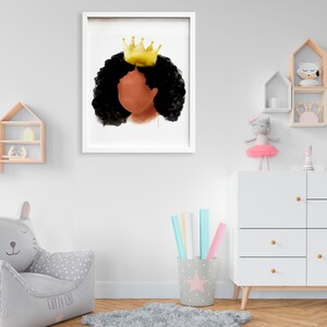 May include: A framed watercolor print featuring a profile of a person with dark skin and black curly hair, wearing a gold crown. The artwork is set against a white background, framed in a white border, and is displayed in a child's room.