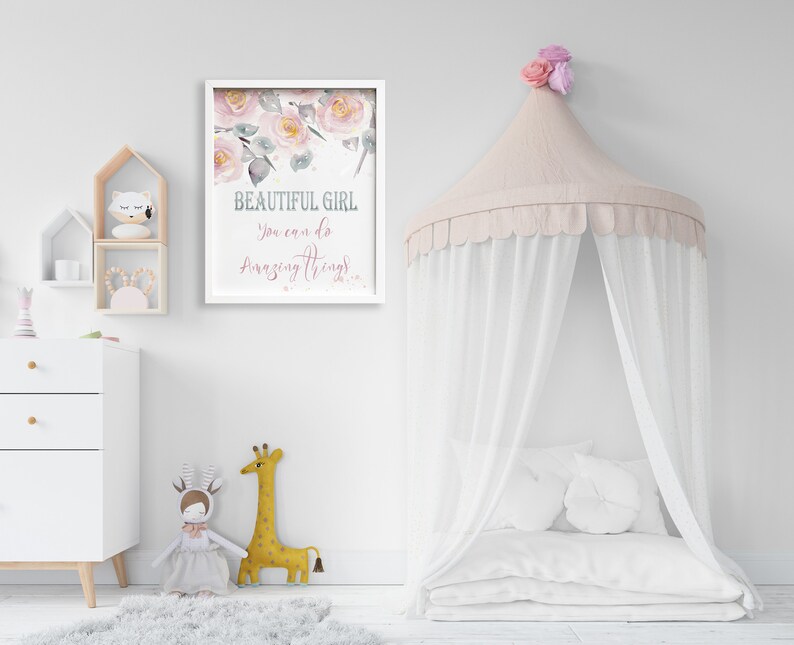 May include: A white framed print with a watercolor floral design and the text "BEAUTIFUL GIRL You can do amazing things!" hanging on a white wall. A white canopy bed with a pink canopy and white pillows is in the foreground.