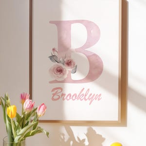 Könnte beinhalten: Ein gerahmter Kunstdruck mit einem großen, blassrosa Aquarellbuchstaben B, der mit zarten rosa Rosen und grünen Blättern verziert ist. Unter dem Buchstaben steht der Name Brooklyn in einer passenden rosa Schreibschrift auf weißem Grund.